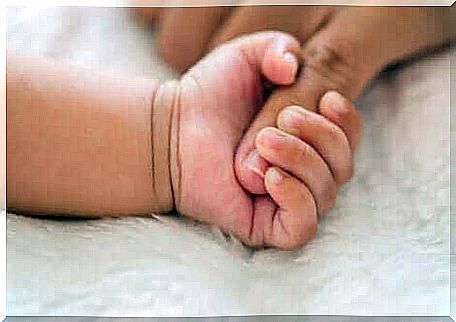 A baby's hand squeezing its mother's finger.